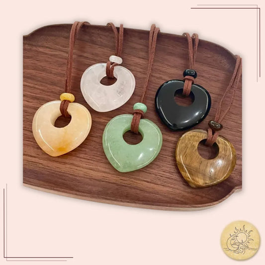 Collection de colliers longs cœur creux en pierres naturelles polies – aventurine, cristal de roche, jaspe jaune, obsidienne et œil de tigre – présentés sur plateau, symbolisant la beauté, l’énergie et la sérénité Aura Cristal.