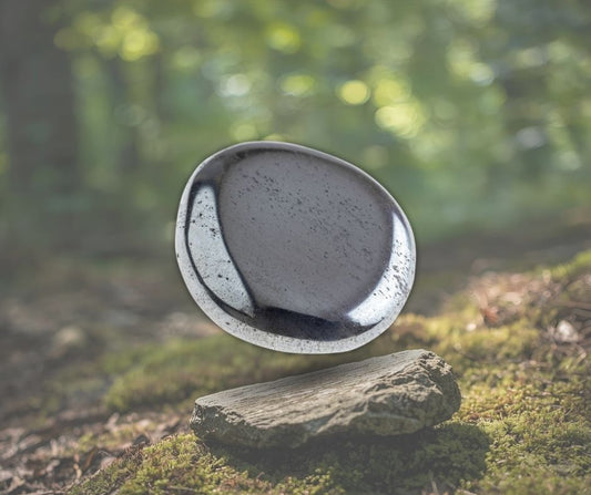 Pierre polie d’hématite grise posée sur un tronc en forêt, symbole d’ancrage, de force intérieure et de protection énergétique – Aura Cristal