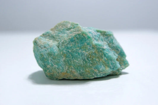 Pierre brute d’amazonite vert d’eau sur fond clair, symbole d’apaisement, d’expression personnelle et d’harmonie émotionnelle – Aura Cristal