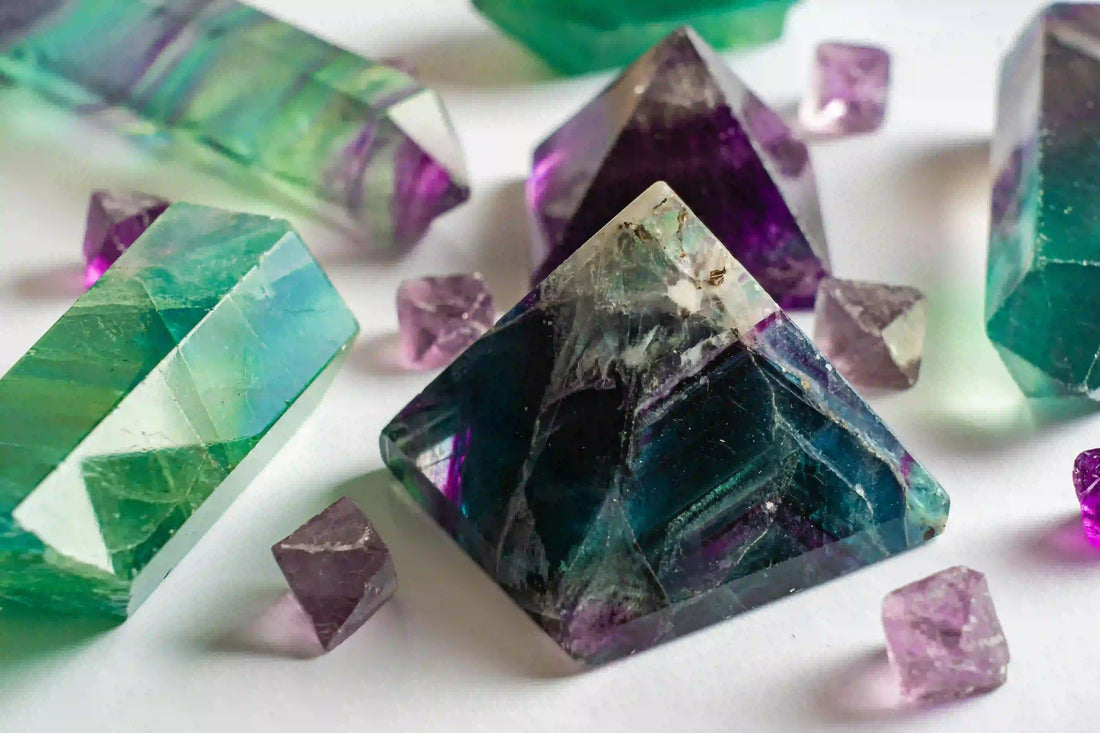 Pyramides et cristaux polis de fluorite verte et violette sur fond clair, symbolisant la concentration, la clarté d’esprit et la protection énergétique – Aura Cristal