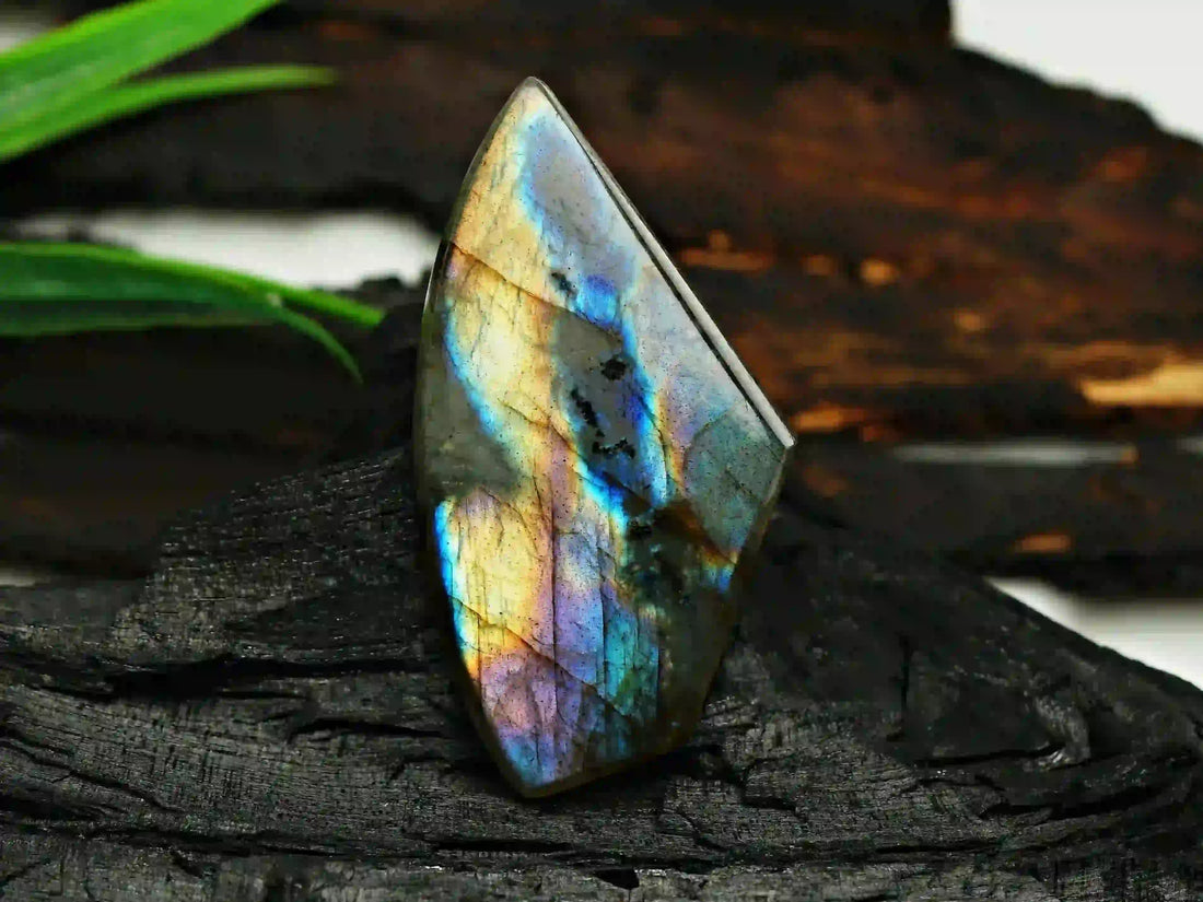 Pierre de labradorite polie aux reflets irisés bleus et dorés, posée sur un fond sombre, symbole de protection, d’intuition et de lumière intérieure – Aura Cristal