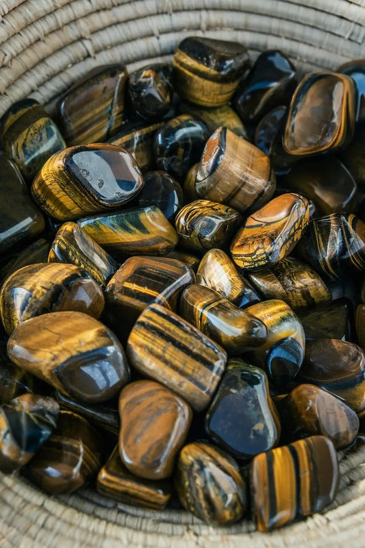 Pierres roulées d’œil de tigre aux reflets dorés et bruns dans un panier, symbole de protection, de courage et de confiance en soi – Aura Cristal
