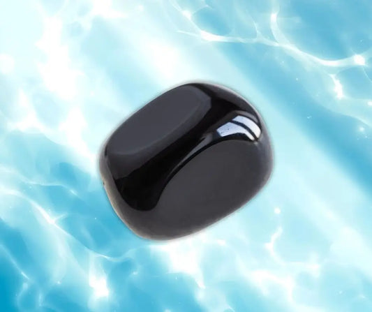 Pierre roulée d’obsidienne noire sur fond lumineux bleu, symbole de protection, d’ancrage et de force intérieure – Aura Cristal
